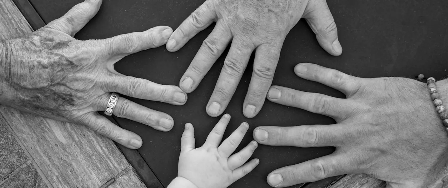 Hands of four generations, from a baby to a great-grandparent, resting together on a table